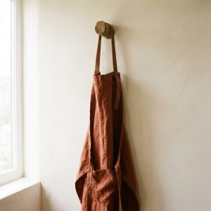 A rust linen apron hanging from a timber peg