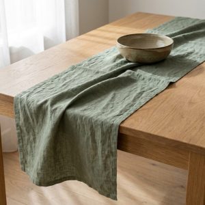 A sage linen table runner across a timber table with a ceramic bowl